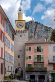 <center> Castellane. </center> La Tour de l'Horloge. Appelée aussi tour de la porte Saint-Michel, elle est datée traditionnellement, avec l'ensemble des remparts de Castellane, de 1359 et des années qui ont suivi. Elle a été transformée en beffroi communal au 18e siècle, avec l'adjonction d'un campanile métallique avant 1775. Elle était autrefois une tour ouverte à la gorge. Mais l'élévation intérieure a été murée à une époque indéterminée. Le mâchicoulis a cédé la place à un beffroi dont la forme est originale. L'édicule de plan carré où se trouve l'horloge est en effet surmonté d'un cylindre maçonné lui-même prolongé du campanile en fer forgé qui porte la cloche. En rez-de-chaussée, la tour, de plan carré, donne le passage à la rue Saint-Victor, grâce à une voûte en berceau en pierre de taille fermée à l'est par un arc brisé dont la naissance est soulignée par un bandeau en quart-de-rond.