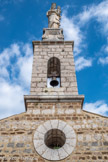 <center> Castellane. Chapelle Notre-Dame-du-Roc.</center> Encore au-dessus, un clocher-mur de section rectangulaire offre une baie en plein cintre abritant une cloche. Le clocher-mur sert également de base à une statue disposée sur un socle galbé.