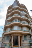 <center>Palais Les Mimosas </center>Architecte Livieri. 1938. Angle Victor Hugo Rivoli. L’entrée sur la bissectrice de l’angle, le marquage du couronnement, le nombre d’étages, la composition des balcons, le duo pierre-béton enduit obéissent à des règles constantes, mais transcrites ici avec une forte originalité et un formalisme presque baroque. L’immeuble alterne la pierre dure blanche en gros bossage rustique filant avec deux tons de bétons enduits, miel et crème, probablement liés au nom de l’immeuble. Le large porche ouvert est également traité dans ces tons, ainsi que ses colonnes polies, de même que le sol étendu en long perron à découvert, composé d’éclats polychromes de carreaux en grès cérame vermiculé, typiquement 1935-1965. L'immeuble compte six étages sur rez-de-chaussée surélevé et sous-sol. L'horizontalité des balcons filants dans l'angle est contrebalancée par l'angle, trifolié, se terminant par un tambour en maçonnerie. La rotonde, marquant un mouvement ondulant, est soulignée par des colonnes, engagées à chaque étage, rappelant l'entrée. L'entrée est large, précédée d'un porche profond en amande, reposant sur quatre colonnes. Garde-corps en maçonnerie surmontés de fers carrés et plats, excepté pour les balcons en corbeille avec garde-corps entièrement en ferronnerie. Une balustrade ceinture les balcons du dernier étage.