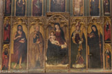 <center>Les Arcs sur Argens : L’église Saint Jean Baptiste.</center>Le panneau central du registre inférieur représente la Vierge portant l'Enfant Jésus sur sa jambe droite. Elle lit un livre ouvert et posé sur sa jambe gauche. La tête de la Vierge et celle de Jésus sont entourées chacune d'une auréole dorée à double cercle. À droite se trouve l'évêque Honorat couvert d'une mitre blanche à bordure rouge et vêtu d'un pallium bleu. Le saint bénit de la main droite et tient une crosse reliquaire de la gauche. À l'extrême droite l'abbé Benoît enveloppé dans une large cape noire, tient un livre. À gauche saint Pierre représenté avec une barbe grise et en manteau jaune, tient les clés du paradis. À l’extrême gauche saint Jean-Baptiste vêtu d'une cape écarlate porte l'agneau divin sur un livre. Les bandes latérales : à droite et de bas en haut, Antoine ermite, Catherine d'Alexandrie en cape écarlate ; à gauche,  Jacques le Majeur en robe noire et manteau rouge, Marie Madeleine en manteau écarlate soulevant le couvercle d'un vase à parfum.