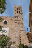 <center>Cathédrale Sainte-Eulalie-et-Sainte-Julie d'Elne</center>L'austère façade occidentale de la cathédrale Sainte-Eulalie confère à l'édifice un aspect de forteresse. Elle est érigée en moellons irréguliers. Deux tours puissantes devaient encadrer l'ensemble. Seul le clocher sud est construit. En pierre, il comprend quatre étages au-dessus de la courtine. À chaque étage et sur chaque face, on trouve quatre baies cintrées ouvertes ou aveugles. Les arcatures aveugles du premier étage sont soulignées par une bande noire en lave d'Olate. Le clocher est couronné par des créneaux. Les grandes arcades ne furent murées que lors de la construction des tribunes. Au-dessus du portail, on trouve une petite baie cintrée, encadrée par un décor de bandes lombardes. Des désordres de maçonneries de l'ensemble roman (XIe au XIIIe siècle) ont été provoqués par le clocher méridional, dont la base a, par conséquent, été confortée au XVe siècle.
