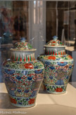 <center>Paire de potiches couvertes</center>Chine, Jiangxi ; Jingdezhen. Dynastie Qing (1644-1911), époque Kangxi (r. 1661-1722)
Porcelaine, émaux de la famille verte. Legs Philippe Jourde, 1913. Fonds Cantini.
Marseille, Château Borély - Musée des Arts décoratifs, de la Faïence et de la Mode.
Cette paire de potiches arbore un décor de la famille verte, appliquant la polychromie de type wucai des « cinq couleurs », manifeste par la combinaison d’un bleu sous couverte et d’émaux polychromes sur couverte. Le décor est formé d’arabesques, dont on trouve l’origine au XIVe siècle, ponctuées de symboles auspicieux. Les « huit objets précieux » - le joyau, la sapèque, le losange, les livres, la pierre sonore, la peinture, les cornes de rhinocéros