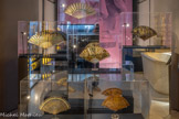 <center>L'éventail, prédilection de l'exotisme.</center>Venu de Chine et du Japon, l’éventail conquiert l’Europe dès le XVIe siècle. Objet de luxe, attribut féminin, il est dans un premier temps réservé aux élites. Dès la fin du XVIIe siècle, les artisans européens, et particulièrement parisiens, ont acquis un savoir-faire qui leur permet de rivaliser avec les importations venues d’Asie.
Les brins sont composés de matériaux rares comme l’écaille de tortue, l’ivoire d’éléphant ou la nacre. La feuille, de peau ou de papier; est peinte de sujets empruntés à l’histoire antique, à la mythologie ou aux événements du temps notamment. L’exotisme constitue une source d’inspiration fréquente pendant plus de deux siècles. Les évocations de l’Occident se mêlent bien souvent à celles de l’Orient pour créer des décors sans équivalent. Les pays lointains apparaissent imaginés, sublimés et parés de merveilleux. La Chine s’avère particulièrement inspirante : elle est campée par quelques éléments récurrents comme des personnages vêtus de longues tuniques et coiffés de chapeaux coniques, par des porcelaines bleues et blanches ou des arbres exotiques tels que les bambous ou les saules pleureurs.
Suggérer le voyage et l’extraordinaire se fait également par des applications inhabituelles. Les décors peints sont rehaussés de mica, de soie, de paille, parfois d’algues ou de plumes, illustrant ainsi une certaine idée des contrées d’Orient.
