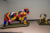 <center>Niki de Saint Phalle</center>L'Aveugle dans la prairie 1974.
Polyester peint au vinyle, armature métallique et grillage Centre Pompidou, Musée national d'art moderne, Paris Achat, 1980
<br>
Parce que Tinguely en était originaire et s'y était établi, mais aussi pour soigner ses problèmes pulmonaires dans une région privilégiée, Niki de Saint Phalle fait, dans les années 1970, plusieurs séjours en Suisse, qui vont l'inspirer pour travailler le motif de la vache. Il en résultera notamment ce groupe sculptural formé de l'animal et d’un homme assis lisant un journal, qu'elle produira à des échelles différentes. L'Aveugle dans la prairie, réalisé dans un très grand format, est acquis par Pontus Hulten pour le Centre Pompidou à l'occasion de la rétrospective de l'artiste de 1980. Si l'homme est aveugle, c'est sans doute parce qu'il ne voit pas la vache joyeusement bariolée, bien plus intéressante que son terne journal.