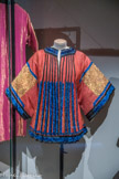 <center>BABANI</center> Veste d'intérieur ou liseuse.
Façonné de soie rouge, broderies de fils métalliques dorés, ruban de satin de soie bleu et noir brodé de fils de soie bleus ; doublure en taffetas de soie jaune. Vers 1905-1906.
Don de la famille Gramont.
Ce modèle provient de la garde-robe de la duchesse de Gramont, née Élaine Greffulhe (1882-1958).
Cette veste qui porte la première griffe de Babani est réalisée dans une jupe chinoise du XIXe siècle aux broderies bleues caractéristiques. Les panneaux devant et dos ont été transformés en manches. Un modèle très proche est reproduit dans Le Figaro-Modes en février 1906.