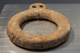 <center>ANNEAU RÉGULATEUR DE TENSION D’AMARRE</center>Ve siècle av.n.è. — Ve siècle
Littoral de Gaza, 2002. Marbre blanc.
Les archéologues ont émis plusieurs hypothèses sur l'utilisation des grands anneaux de pierre connus depuis l'âge du Bronze ancien (3200 av.n.è.). Un anneau en marbre, dont la partie supérieure est percée de deux petits trous, est interprété comme un dispositif d’amarrage régulant la tension du câble reliant l'ancre au navire.
Autorité Nationale Palestinienne, ancienne collection Jawdat Khoudary, Gaza. Dépôt au Musée d'art et d'histoire, Ville de Genève.