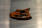 <center>FRAGMENT DE RÉCIPIENT (PYXIDE?) : CHIEN ET PANTHÈRE SE FAISANT FACE</center>Production grecque de l’Attique, période perse, début IVe e siècle av.n.è.
Découvert à Gaza, Blakhiya (antique Anthédon)
Céramique attique à figures rouges
Ce fragment est décoré selon la technique de la «figure rouge» et met en scène l’affrontement d’un chien et d’une panthère. La représentation du félin est fidèle à la convention archaïque : visage de face, corps de profil. Pour le chien, au contraire, sa posture est réaliste. Les points sur le chien et la panthère suggèrent leur fourrure.
