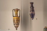 <center></center>2. Vase à parfum de type « alabastron »
Epoque ptolémaïque, IIe s. av. J.-C.- Ier siècle av. J.-C.
Verre polychrome
Paris, musée du Louvre, département des Antiquités grecques, étrusques et romaines. <br>5. Amphorisque
Fin du IIe - début du Ier siècle avant J.-C.
Verre sur noyau.
Genève, Fondation pour Gandur pour l’art.<br> Outre les pièces d’orfèvrerie, les Ptolémées et leur Cour apprécient la vaisselle de luxe fabriquée en Égypte selon des traditions séculaires. Le pays est fameux pour ses vases de pierres, ses verreries multicolores et ses objets en «faïence». Intailles et camées, souvent montés en bagues, témoignent de la virtuosité des artisans.