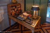<center>Grand cabinet </center>Bureau plat couvert en cuir et son cartonnier, plaqués de bois de satiné et de marqueterie de citronnier et d'amarante. Les quatre pieds fuselés sont pris dans des sabots et marqués en partie supérieure par des denticules en bronze doré. On distingue deux tiroirs et faux tiroirs en ceinture garnis d'un fond mosaïqué à fleurettes et encadrés par un jonc rubané. Les angles sont enrichis d'une applique de bronze en drapé retenu par des anneaux.
Le cartonnier, posé en bout, forme une caisse à sept compartiments surmontée d'une galerie. Elle reprend un motif mosaïqué en plein et les arrêtes sont protégées par du bronze doré. 1771-1794. Mathieu-Guillaume Cramer, d'origine allemande, est reçu maître ébéniste à Paris le 4 septembre 1771. Son atelier se trouvait d'abord au faubourg Saint-Antoine puis rue du Bac. Cramer est connu pour ses marqueteries de rosettes sur fond de bois jaune dont cet ensemble est un exemple. <br>Paire de statues (statuettes) : chevaux cabrés. 17e siècle. Cette paire de chevaux, fondue au XVIIe siècle, témoigne du goût de l'époque pour les petits bronzes, meublant notamment les cabinets, et pour l'observation de la nature.