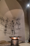 <center>L’église Sainte Jeanne de Chantal </center>L’autre vasque, cuve baptismale, reçoit l’eau nécessaire au baptême. Les murs des chapelles latérales se couvrent de grisailles représentant des scènes du Nouveau Testament. L’artiste Jean-Louis Sauvat les dessine au fusain. Ces grisailles servent de fond aux premières fresques vidéo-projetées jamais réalisées dans une église. Baptême de Jésus.