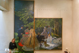 <center></center>Le Déjeuner sur l'herbe, 1865-1866 par Claude Monet. La genèse de ce tableau, dont le sujet fait référence au fameux Déjeuner sur l’herbe (1863) de Manet, remonte au printemps de l’année 1865.
Précédé d’esquisses faites en plein air à Chailly-en-Bière en bordure de la forêt de Fontainebleau, élaboré dans l’atelier de la rue Furstenberg qu’il partageait avec Bazille 1 (qui a posé pour son ami) et où Courbet vint le voir (lui aussi est représenté, assis, à terre), le tableau était fort avancé avant la fin de l’année. Toutefois Monet ne le présenta pas au Salon de 1866 ; l’œuvre demeurée inachevée fut roulée et laissée en gage à des créanciers de l’artiste qui ne put la racheter qu’en 1884. La toile ayant souffert, Monet prit la décision de la découper, faisant mettre sur châssis la partie centrale qu’il accrocha dans sa maison de Giverny. Aujourd’hui, une esquisse réduite mais très élaborée conservée au Musée des Beaux-Arts Pouchkine de Moscou permet de reconstituer l’immense composition (environ 4,00 m sur plus de i m de longueur), chef-d'œuvre d’un artiste de vingt-cinq ans.