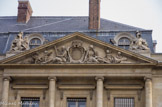 <center>Le Palais Royal.</center> Le fronton en pierre couronnant le pavillon est représente La Prudence et la Libéralité.  En 1871, l’incendie du Palais-Royal détruisit l’aile droite de la Cour de l’horloge et les étages du bâtiment central. C’est l’œuvre de Jules Franceschi, d’après Pajou (1825-1893) qui l’a exécutée vers 1872/1874 en imitation du bas-relief original de 1765. Au-dessus, deux Trophées, œuvres d’Adolphe Martial en 1874. Ces trophées représentent des torses affublés de tout l’équipage pour mener une bataille, un combat.