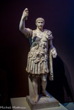 <center>Trajan.</center>C’est une statue reconstituée : les bras sont modernes, la tête de est celle de Trajan et la cuirasse est de son époque. Sous Trajan, l’empire a atteint ses frontières les plus étendues. Trajan est célèbre pour ses campagnes, en particulier contre les Daces. Tous les empereurs se sont fait représenter en chef des armées. Le portrait est assez réaliste, il ne ressemble pas à Auguste. Ce qui est le plus spectaculaire est la cuirasse. On y voit des motifs destinés à faire peur, d’autres pour montrer les conquêtes de l’empereur, des captifs enchaînés comme sur les arcs de la région, les victoires qui vont accrocher les boucliers autour d’un trophée et au-dessus, le duocéum qui est sensé diffuser dans tout le monde connu l’écho des victoires de l’empereur. Trajan a adopté sur son lit de mort Hadrien, par la volonté de son épouse Clotilde qui voulait que ce soit lui qui lui succède.