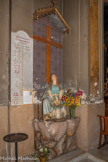 <center>L'église de La Trinité. </center> Statue de Sainte Marie-Madeleine en pleurs au pied de la Croix. Socle et Statue en carton-pierre polychrome. Date : fin 19e - début 20e siècle, avant 1921. Née à Magdala (d'où son nom) elle s'attache à Jésus qui lui pardonne sa vie dissolue.
Elle est au pied de la croix au Calvaire, près de saint Jean et de la Vierge Marie, la mère de Jésus. C'est ainsi qu'elle est représentée ici, avec à ses pieds le pot d'aromates pour l'embaumement du corps. Selon la tradition provençale les saintes femmes auraient débarqué à Marseille, en 42, après la persécution d'Hérode; accompagnées de quelques autres disciples. Puis Marie-Madeleine se serait retirée dans le massif de la Sainte-Baume, où elle aurait vécu en ermite les trente dernières années de sa vie. A sa mort, elle aurait été ensevelie à Saint-Maximin.