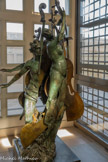 <center> Apollon et Daphné</center>Arman (1928-2005). 1987 Bronze 220x97x80 cm. Arman s'est rendu célèbre dès les années 1960 avec ses accumulations, empilements ou juxtapositions d'un même objet de consommation courante en de multiples exemplaires : fers à repasser, appareils photo, téléphones, haches, ustensiles de cuisine, etc. Cette œuvre se rattache à une autre série, plus tardive, dans laquelle Arman revisite à sa manière iconoclaste les grands chefs-d'œuvre de l'histoire de la sculpture. En l'occurrence, l'œuvre-source est et Daphné (Galerie Borghèse, Rome), extraordinaire groupe statuaire réalisé par Le Bernin en 1622. Le dieu Apollon poursuit de ses assiduités la nymphe Daphné - il a déjà la main posée sur sa hanche, mais elle parvient à lui échapper en se métamorphosant en laurier.
S'il reste fidèle au Bernin dans la composition générale et l'attitude des personnages, Arman livre une version très personnelle à un triple titre : le marbre a laissé place au bronze ; l'œuvre est littéralement tronçonnée, ce qui accroît encore l'impression de mouvement déjà présente dans l'original, d'une théâtralité toute baroque ; enfin, dans une démarche pleine de poésie, l'artiste a intercalé des sections d’un violoncelle, lui dont l’univers est rempli de références à la musique.