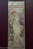 <center>La Dame aux Camélias</center>Cette affiche est la première créée par Mucha dans le cadre du contrat qu’il signe en 1895 avec Sarah Bernhardt, après le succès de La Dame aux Camélias est écrite à l’origine comme un roman de 1848 par Alexandre Dumas fils adapte pour la scène en 1852. Sarah Bernhardt tient le rôle principal de Marguerite, une courtisane qui vit un amour tragique car elle se meurt de la tuberculose. L’actrice est ici représentée affaiblie tout de blanc vêtue, s’appuyant contre une balustrade sur un fond parsemé d’étoiles. Les fleurs sont mises à l’honneur, comme les camélias blancs, fleurs préférées de l’héroïne, ou les roses épineuses symbolisant le sacrifice ultime de l’amour, thème de la pièce. La courtisane au destin tragique sera le rôle le plus demandé à Sarah Bernhardt qui le jouera plus de troois mille fois au cours de sa carrière.