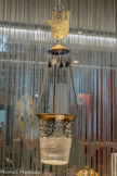 <center>Lampe de synagogue</center>1900 1950
Maroc
Verre moulé et doré, cuivre gravé
Cette lampe avec l'inscription hébraïque « Que sa mémoire soit bénie » est dédiée à une personne disparue. La suspension comporte une étoile de David et une khamsa, symbole protecteur en forme de main.
Le récipient était garni d’huile dans laquelle trempait une mèche, ou bien rempli d’eau où flottait une bougie.