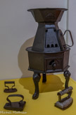<center>Gaillac</center>Fer à repasser 19e-premier tiers du 20e siècle. Fer (moulé) ;  métal (émaillée). Apparus à la fin du 17e siècle, les premiers fers à repasser furent bien réalisé en fer. Les modèles exposés ici sont des fers «  plaque » en fonte, qui avait l'inconvénient de refroidir vite et d'être souvent sali par la suie. Des fers « lingot » ou « à bateau » furent donc inventé :  leur semelle creuse pouvait accueillir un lingot de fonte chauffé ou des braises. Le fer à repasser électrique fut quant à lui créer en 1882 et le premier fer à vapeur en 1963. 
Poêle pour chauffer les fers à repasser. Dernier tiers du 19e -  premier tiers du 20e. Fonte (coulée)