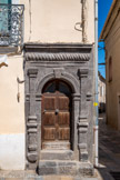 <center>Vias</center>Place du 14 juillet. Les rues de Vias abritent un nombre important de très belles portes sculptées du début du XVIIème siècle. Ces portes taillées dans la roche volcanique, le basalte, se caractérisent par l'harmonie de leurs proportions et l'absence de fioritures. Une sobriété sans doute en partie due à la dureté du matériau utilisé. Leur décor de pilastres, d'entablement torique, leurs clefs ornées de motifs végétaux rappellent les portes gravées par le célèbre architecte Sébastien Serlio. Les maçons locaux n'ont pas imité les modèles du maître, mais ont pulsé dans ses recueils divers éléments qu'ils ont juxtaposés pour créer leurs propres ouvrages. Porte dite serlienne. Dans l'angle de la place, près de la fontaine, s'ouvre une porte piétonne : deux pilastres surmontés de chapiteaux doriques encadrent une baie en plein cintre. Ils supportent un entablement sur lequel court une frise, sorte de bandeau arrondi où s'enroule en spirale un
ruban. Une clé décorée d'un écusson timbre le haut de l'arcade. Sur cette clé, se lit l'inscription suivante : G. M. 1603 où lettres et chiffres sont en plomb rapporté. Il faut souligner les particularités des pilastres : dotés de très hauts piédestaux qui les rattachent à la Renaissance, ils coupent les moulures qui soulignent les impostes de l'arc de la porte.