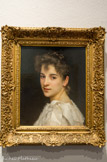 Portrait de Gabrielle Cot. WILLIAM BOUGUEREAU (1825 1905). Huile sur toile, 1890. 
Il s'agit ici du portrait de Gabrielle Cot, fille du peintre Pierre-Auguste Cot (1837 -1883) et de Juliette Duret, fille du sculpteur Francisque-Joseph Duret (1804 -1865). Malgré les vingt ans d'écart qui les séparaient, le peintre Bouguereau et le sculpteur Duret étaient très étroitement liés ainsi que leurs ramilles, entraînées dans le sillage de cette amitié.
Le modèle ne pose pas. Tournée vers le peintre, comme arrêtée dans son mouvement, elle le regarde droit dans les yeux. La jeune femme connaît bien le peintre. Elle n'est donc pas intimidée et son regard est confiant et doux.
Le buste se détache sur un fond sombre et uni qui met en relief les tons crème et les aspects contrastés des tissus de sa robe où s'opposent le lustré du ruban de satin et le frisottis des dentelles. Aucun décor, aucun effet ne distrait l'observateur de sa rencontre avec cette jeune femme dont l'attitude est naturelle et l'expression dégagée. L'extrême précision du dessin, l'aspect lisse de la peinture et la sobriété du coloris dont est absente toute couleur franche, rapprochent cette représentation de l'art de la photographie.