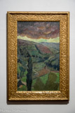 La Pluie. PAUL SERUSIER (1863 – 1977). Huile sur toile.
Artiste ultra doué, Paul Sérusier se trouve un octobre 1888 à Pont-Aven où sous la houlette de Gauguin, il peint Paysage au bois d’Amour. Ce dernier l’encourage à peindre en plein air des couleurs franches. De retour à Paris, il montre son œuvre, également appelé Le Talisman, à ses amis Maurice Denis, Bonnard, Ibels et Ranson qui se réunissent autour. Ensemble, ils fondent le groupe des Nabis, sans contour défini ni unité stylistique, Sérusier, le « Nabi à la barbe rutilante », retourne régulièrement Bretagne. Durant l’été 1899 avec Filiger, Gauguin et de Haan, il est pensionnaire de Marie Henry au Pouldu. Après un séjour à Pont-Aven où il rencontre Verkade et Ballin en 1891, il s’installe au Huelgoat, jusqu’à 1893.
La Pluie rappelle La Barrière, les thèmes, très simples, sont comme un retour aux sources. Ici, le paysage vallonné montre des parcelles de culture, toutes vertes, plus ou moins claires, délimitées par des haies très sombres. Le cyprès du premier plan renforce la verticalité de la composition. Derrière les nuages très sombres percent le soleil. La pluie n’est visible que par les petites touches fragmentées et au obliques dont use Sérusier.