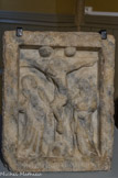 <center>La Casa Xanxo. </center>Le calvaire de la Font del Carmes. Ce bas-relief est sculpté dans un marbre blanc veiné de bleu des carrières de Céret Il daterait de la fin du XIIIe siècle ou du début du XIVe siècle et porte l’inscription Bernardus Miri. Il représente un Calvaire, une scène de la Crucifixion. Jésus sur la croix est encadré par la vierge Marie, à gauche, et saint Jean l’Évangéliste tenant un livre, à droite. Le soleil et la lune apparaissent de part et d'autre du sommet de la croix.