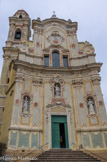 <center>San Giovanni Battista.</center> La décoration de la façade de 1768 est l'oeuvre de Michelle Mazetti. Statues de l'évêque st Nicolas, de saint Jean Baptiste et d'un religieux.