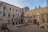 <center>Cour d'honneur, palais neuf </center>Clément VI, dès le début de son pontificat, en 1342, fit raser les maisons et édifices situés près du palais vieux. Ces bâtiments délimitaient la place des Cancels et c'est sur cet emplacement que fut établie la « Cour d'Honneur. C'était au XIVe siècle, le lieu de passage, de rendez-vous et d'attente où se pressaient tous ceux qui étaient admis au palais. De la fenêtre de la « Grande Audience », qui la surplombe sur le côté droit, le souverain pontife apparaissait à la foule et lui donnait sa bénédiction. C'est un carré de 1 800 mètres carrés environ qui est borné au sud et à l'ouest par le palais neuf. En son centre se trouvent les vestiges de la salle d'audience de Jean XXII et le puits, profond de 29 mètres, qu'Urbain fit creuser.
