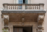 <center>Le palais de justice.</center> Le décor au centre : le balcon et la balustrade sont en pierre car nous sommes au XVIIe. Sous le balcon, des lions avec des draperies dans la gueule, au centre, un Mascaron.